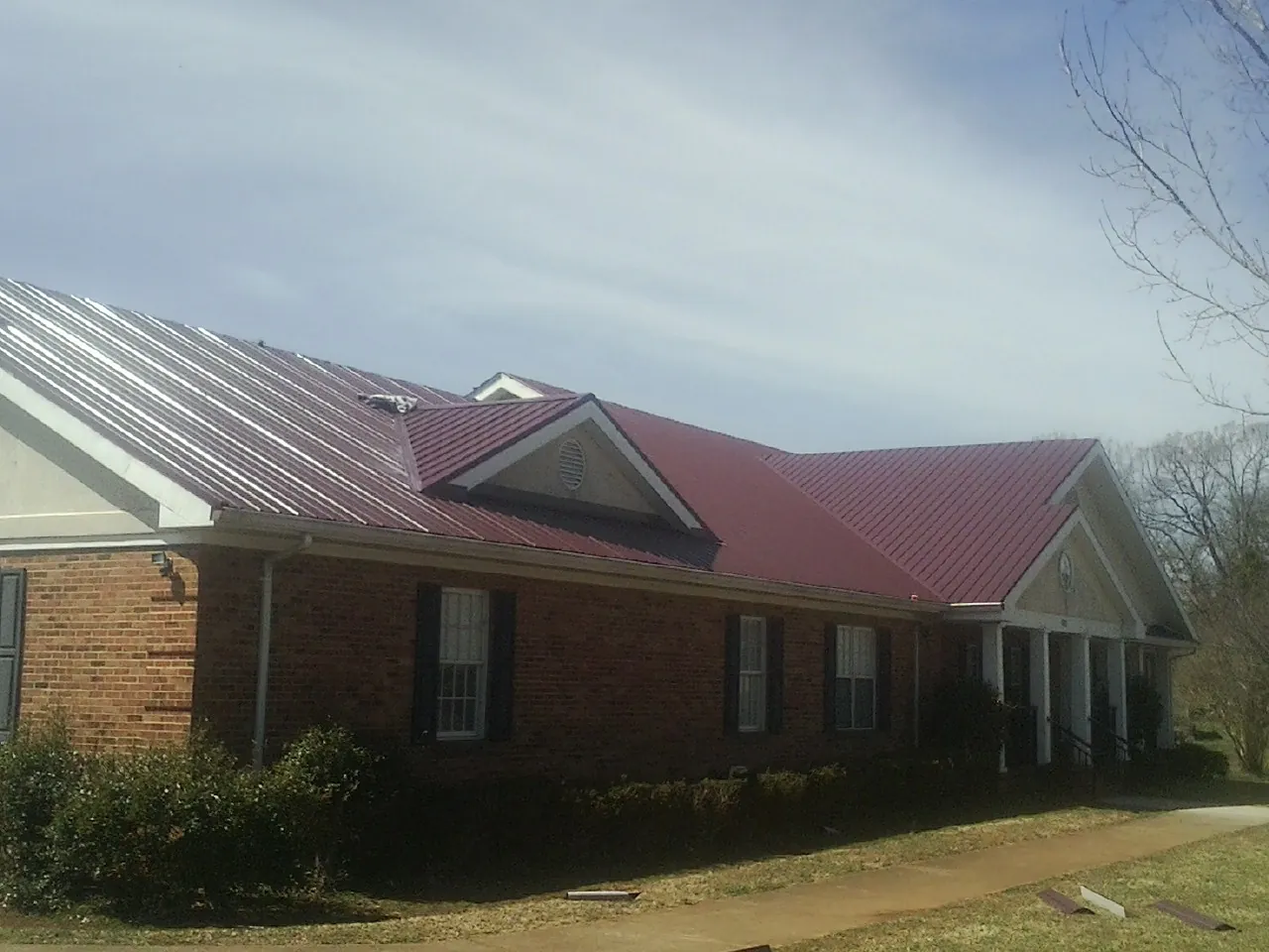 Red metal roof with gabled entries on a long brick building, from a Hail Damage Roof Repair job in Calera