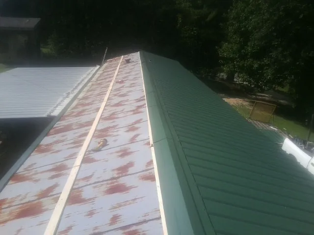 Old rusted panels beside newly installed green metal roofing — Wind Damage Roof Repair by Roofing Brothers in Calera