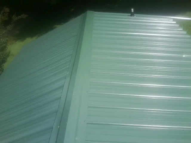 New green metal panels meeting at the ridge of a roof — Flat Roof Repair work by our crew in Calera
