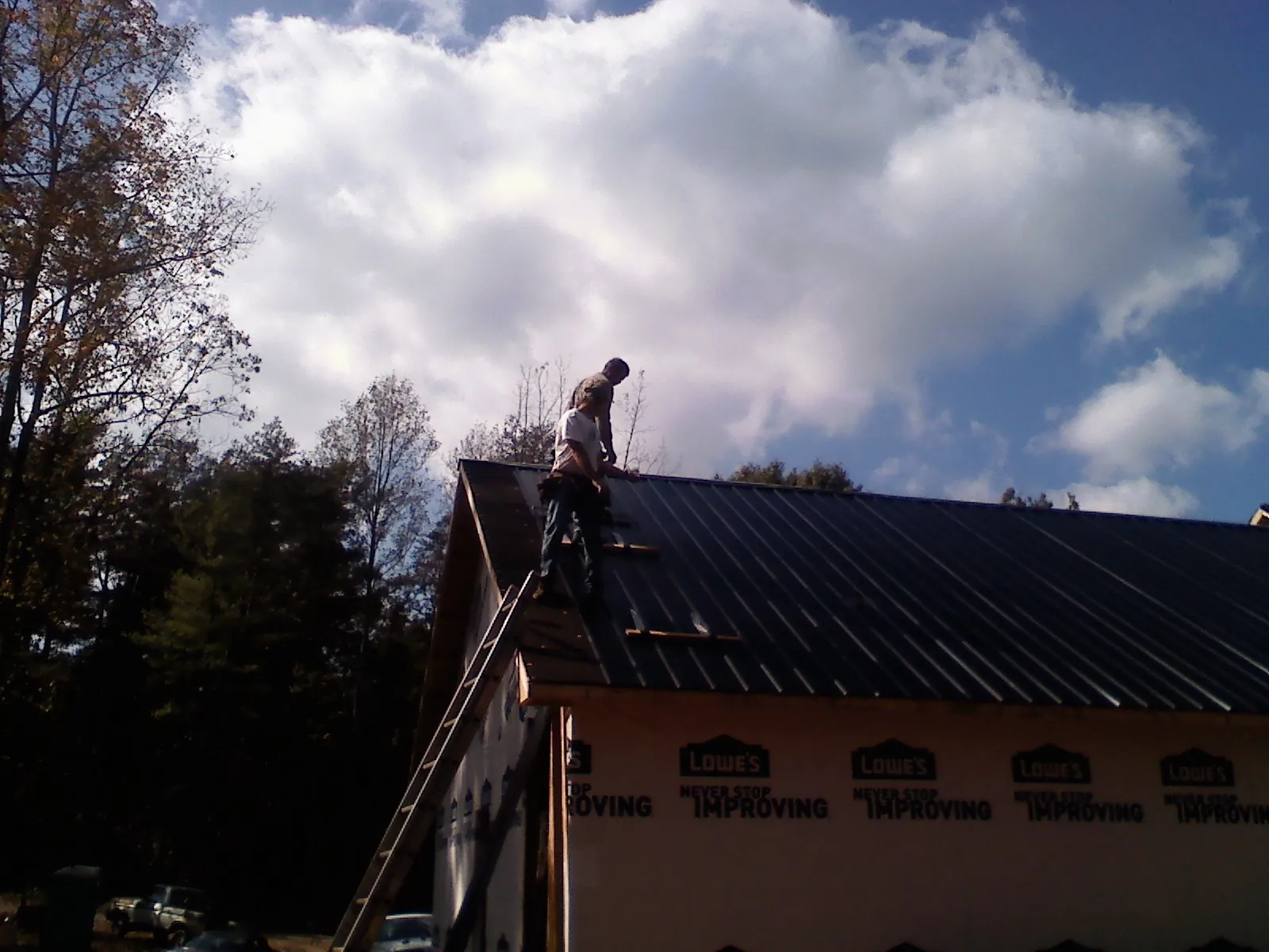 Roofer fastening dark metal panels high against a cloudy sky, from a Roof Inspection job in Calera