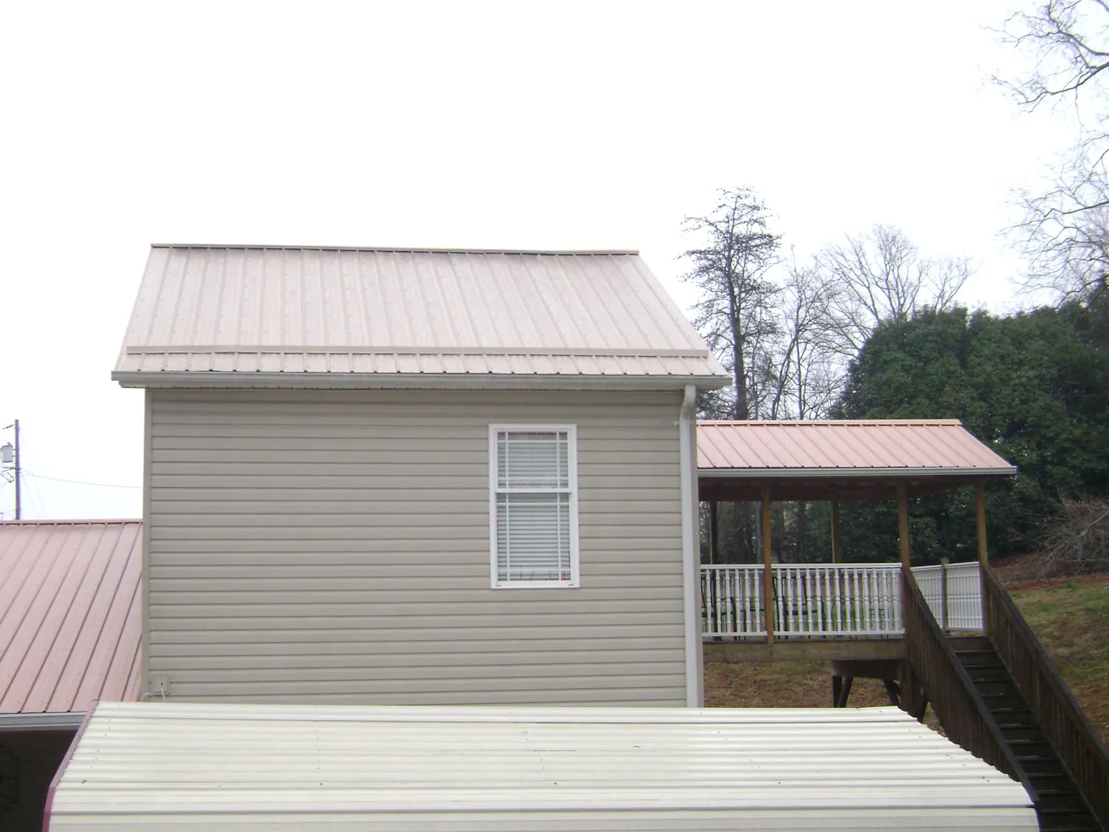 Tan metal roofs on a two story addition and attached porch, from a Roof Replacement job in Calera